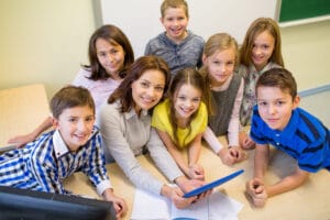 education, elementary school, learning, technology and people concept - group of school kids and teacher with tablet pc computer in classroom