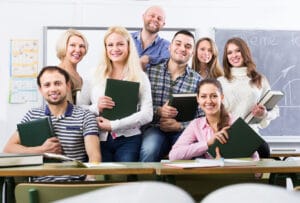 Portrait of friendly teacher and adult positive students in classroom