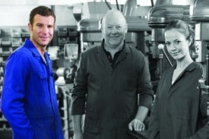 02A157GQ Three machinists in workspace by machine talking