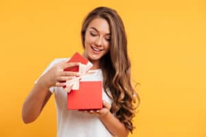 Portrait of a happy smiling girl opening a gift box isolated over yellow background