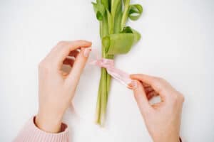 Young woman tying a ribbon on a bouquet of pink tulips. Top view, white background, text copy space.