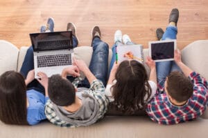 Top view of a four young people, students are sitting on sofa with laptop and tablet, are studying.